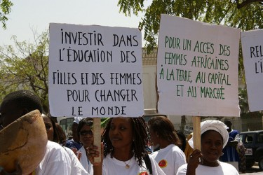 Posters read: (l) "Invest in education of girls and women to change the world" and (r) "For access of African women to land, capital and markets". Image by Flickr user CNCD-11.11.11 (CC BY-NC-SA 2.0).