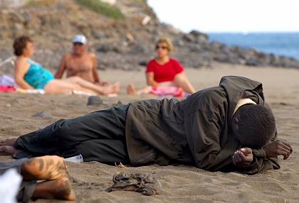 Измученный потенциальный мигрант отдыхает рядом с загорающими туристами на пляже недалеко от Туинехе, на острове Фуэнтэвентура (испанские Канарские острова), фотография пользователя Flicr Noborder CC-BY-20